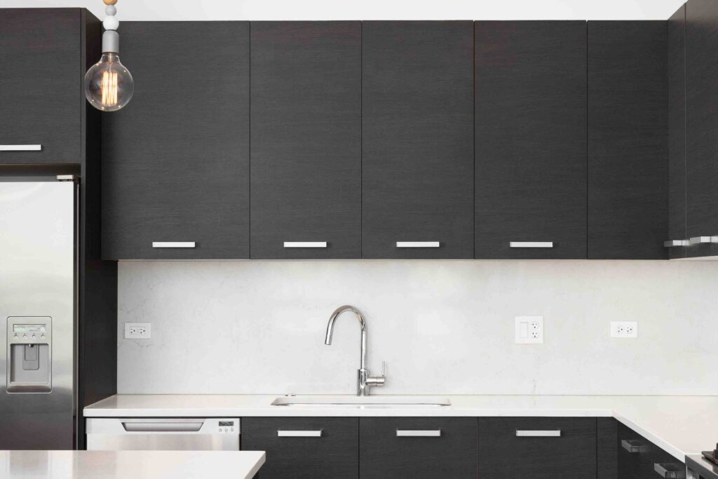 A kitchen sink detail in a modern kitchen with dark wood cabinets, marble countertop and backsplash, and a chrome faucet.