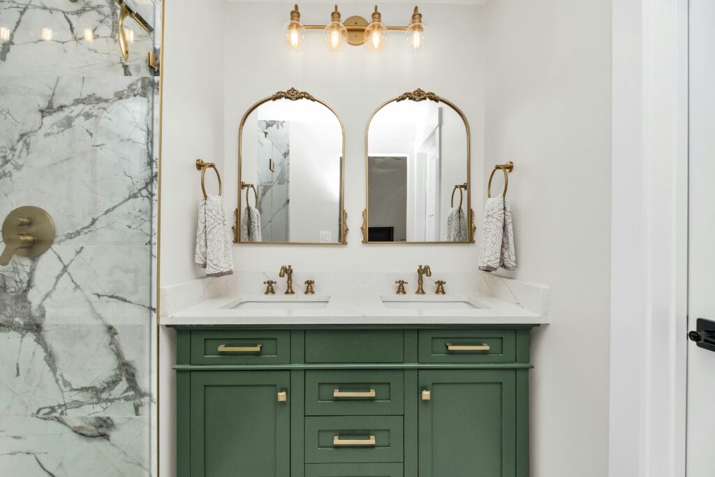 Los Angeles bathroom remodel featuring green vanity with brass fixtures and marble backsplash